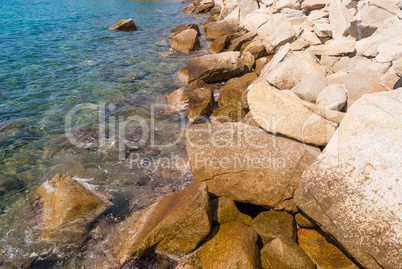 Transparent sea water washes the rocks on the shore covered with