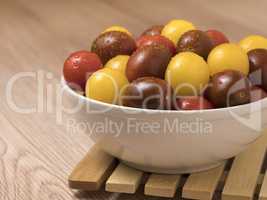 Cherry tomatoes in ceramic bowl on wooden background.