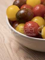 Cherry tomatoes in ceramic bowl on wooden background.