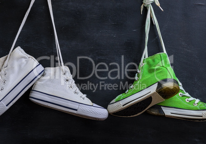 two pairs of used textile shoes hang on a black background, clos