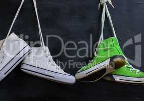 two pairs of used textile shoes hang on a black background, clos