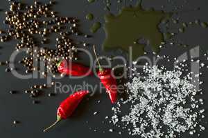 Chili peppers, oil, salt and pepper over a dark background