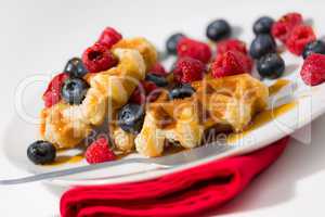 Close-up of waffles with berries and maple syrup on a white plat