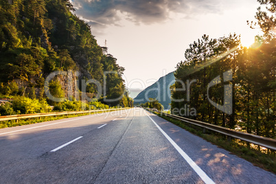 Road in the mountain forest in Alps and sunshine