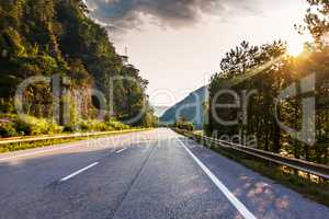 Road in the mountain forest in Alps and sunshine