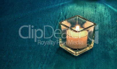 White glowing candle on an aqua silk tablecloth