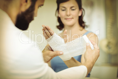 Physiotherapist putting bandage on injured hand of patient