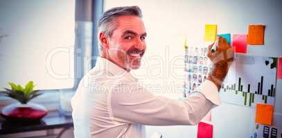 Happy mature businessman making strategies on whiteboard in creative office