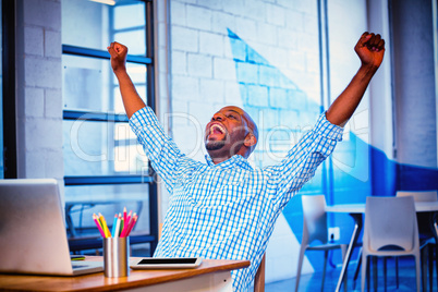 Excited man sitting on table with digital tablet and laptop