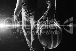 American football player standing with helmet against black background