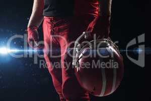 American football player standing with helmet against black background