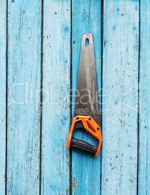 hand saw is hanging on a nail on a blue wooden wall