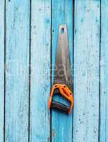 hand saw is hanging on a nail on a blue wooden wall