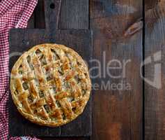 Baked whole round apple pie on a rectangular old brown board