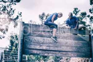 Fit man and woman climbing on wooden wall during obstacle course