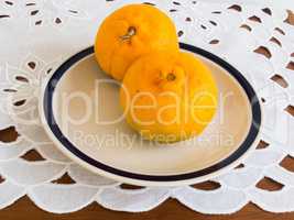 Two ripe tangerines on a porcelain dish.