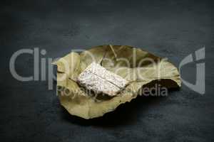 Raw tempeh wrapped in leaf, dark background.