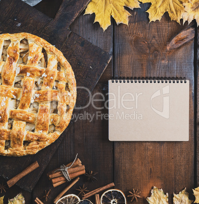 baked apple pie on a board and a notebook with a blank page for