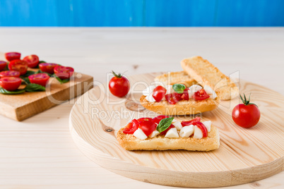 Italian crostini with mozzarella, cherry tomatoes and basil over a cutting board