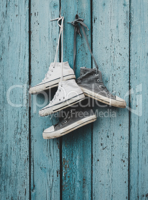 two pairs of old worn textile sneakers hang on a nail