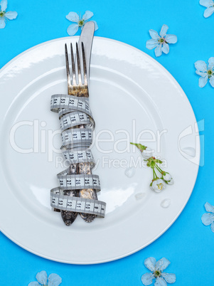 fork with a knife wrapped in a measuring tape lie on a white rou