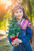 Cute Mixed Race Young Girl Holding Small Christmas Tree Outdoors