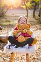 Cute Young Mixed Race Girl Hugging Teddy Bear Outdoors