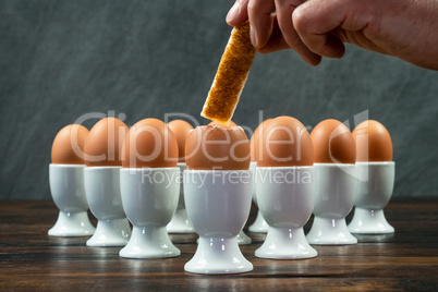 Hand Dipping Toast Soldier Into Boiled Eggs in Egg Cups on a Tab