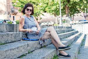 Woman is sitting with coffee cup on the stairs