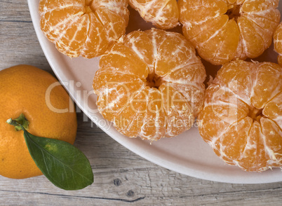 Fresh ripe peeled tangerine in a dish on a wooden background.