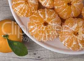 Fresh ripe peeled tangerine in a dish on a wooden background.