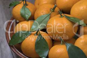 Fresh ripe tangerines with leaves in bowl on a wooden background