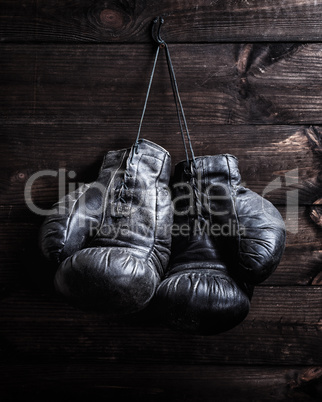 pair of very old shabby black leather boxing gloves hanging on a