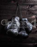 pair of very old shabby black leather boxing gloves hanging on a