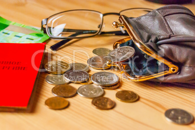 Small bills and coins, an open purse and glasses next to the pensioner's certificate are on the table
