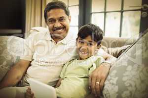Portrait of smiling boy with grandfather holding digital tablet while sitting at home