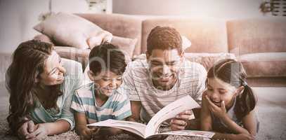 Parents and children lying on rug and reading book in living room