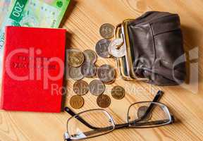 On the table are small bills and coins, an open purse and glasses next to the pensioner's certificate. Inscription: "Pension certificate"