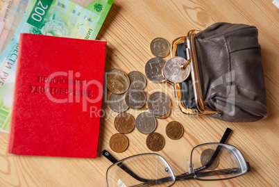 On the table are small bills and coins, an open purse and glasses next to the pensioner's certificate. Inscription: "Pension certificate"