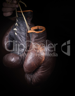 hand holds a pair of brown very old boxing gloves