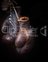 hand holds a pair of brown very old boxing gloves
