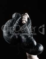 raised up man's hand holds a pair of old black leather boxing gl