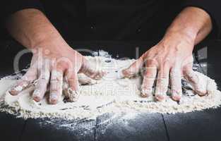 white wheat flour on a black wooden table and two male hands