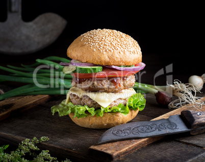 cheeseburger with vegetables on a brown old wooden board