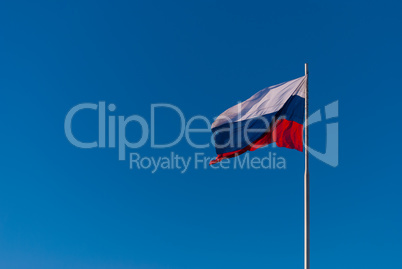 The national flag of Russia on the flagpole fluttering wind against the blue sky. Russia