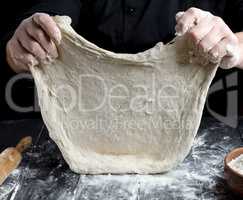 Chef in black jacket, kneads dough from white wheat flour