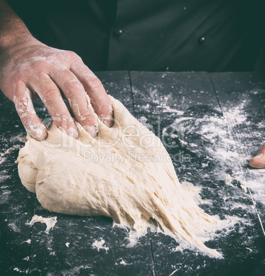 Chef in black jacket, kneads dough from white wheat flour