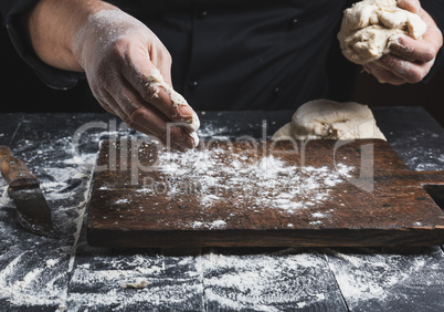 chef in black jacket, kneads dough made from white wheat flour