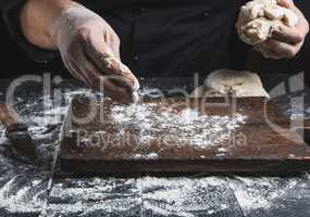 chef in black jacket, kneads dough made from white wheat flour