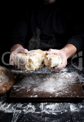 male hands breaking open baked bread in half over black wooden t